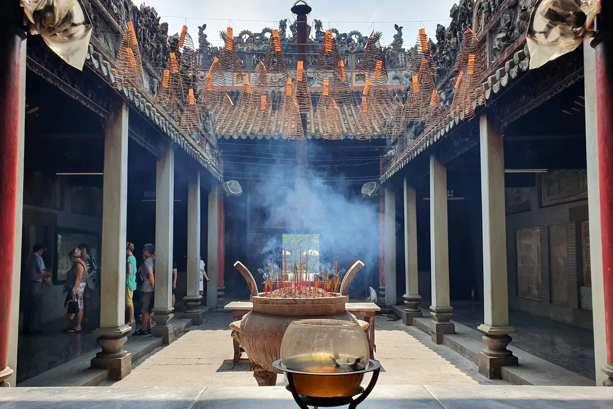 Spiral incense coils hang above a smoking bronze urn in a courtyard temple in Saigon.