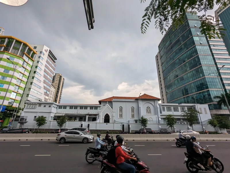 Motorbikes and cars pass a small colonial-era church nestled among modern high-rise towers in Ho Chi Minh City.