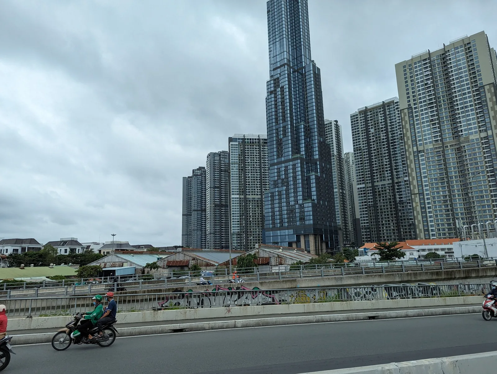 Motorbikes ride past a skyline of high-rise towers including a landmark skyscraper in Ho Chi Minh City.