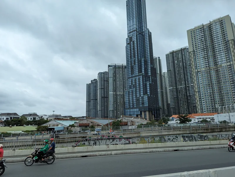 Motorbikes ride past a skyline of high-rise towers including a landmark skyscraper in Ho Chi Minh City.