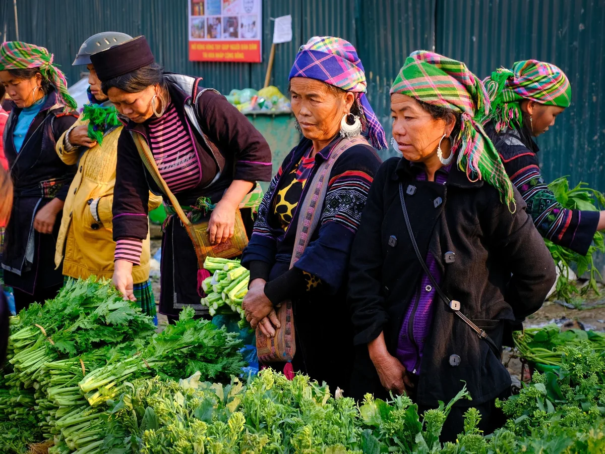 Hmong women in colorful traditional headscarves shop for fresh vegetables at a market in Sapa.