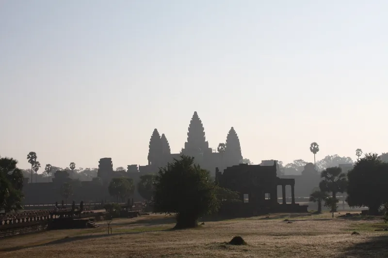 The silhouetted towers of Angkor Wat rise above trees in the hazy morning light near Siem Reap.