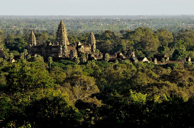 The towering spires of Angkor Wat rise above a dense green forest canopy near Siem Reap.