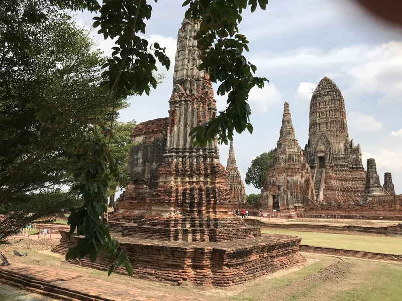 Weathered stone prangs of Wat Chaiwatthanaram rise among trees at Ayutthaya's historical park.