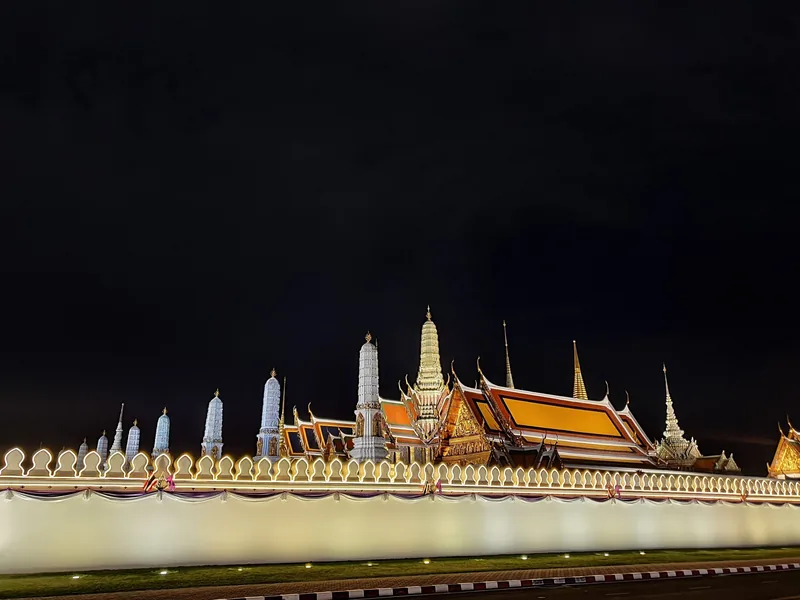 Illuminated spires and rooftops of the Grand Palace glow against the night sky in Bangkok.