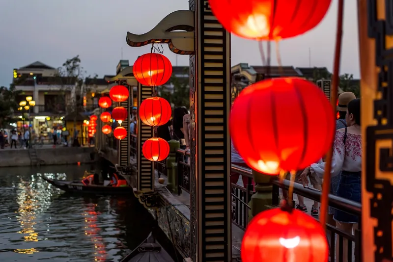 Red silk lanterns glow along a riverside pavilion at dusk in Hoi An