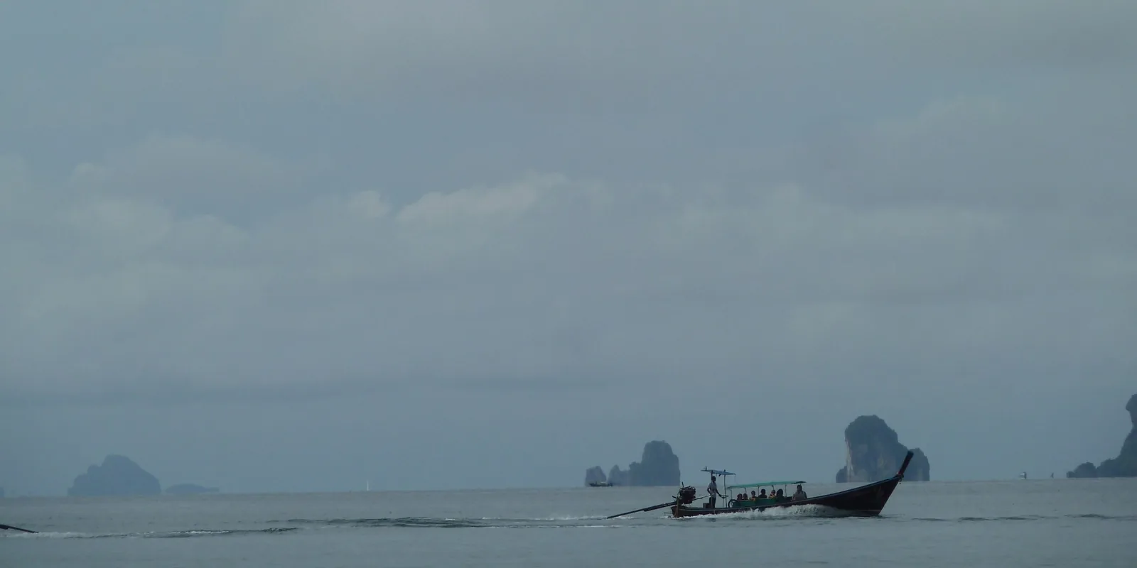 A long-tail boat carries passengers across calm sea past limestone karst islands near Krabi, Thailand.