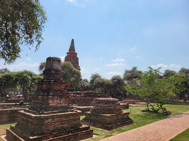 Weathered brick chedis and ruins stand amid green grass at a historic temple site in Ayutthaya, Thailand.