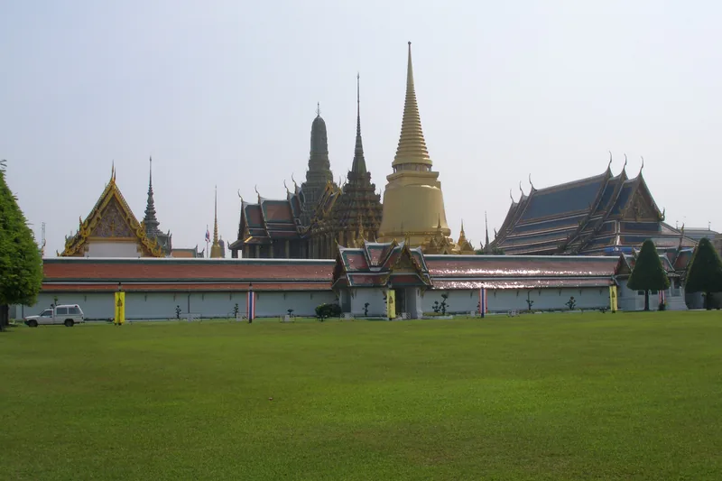 Ornate spires and golden chedi of Wat Phra Kaew rise behind the Grand Palace's white walls in Bangkok.