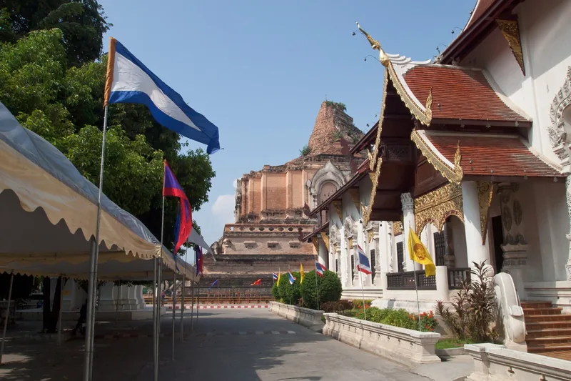 Ancient brick chedi and ornate temple hall stand behind flags at Wat Chedi Luang in Chiang Mai.