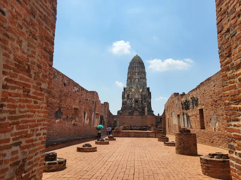 Brick ruins frame the tall central prang of Wat Ratchaburana in Ayutthaya under a blue sky