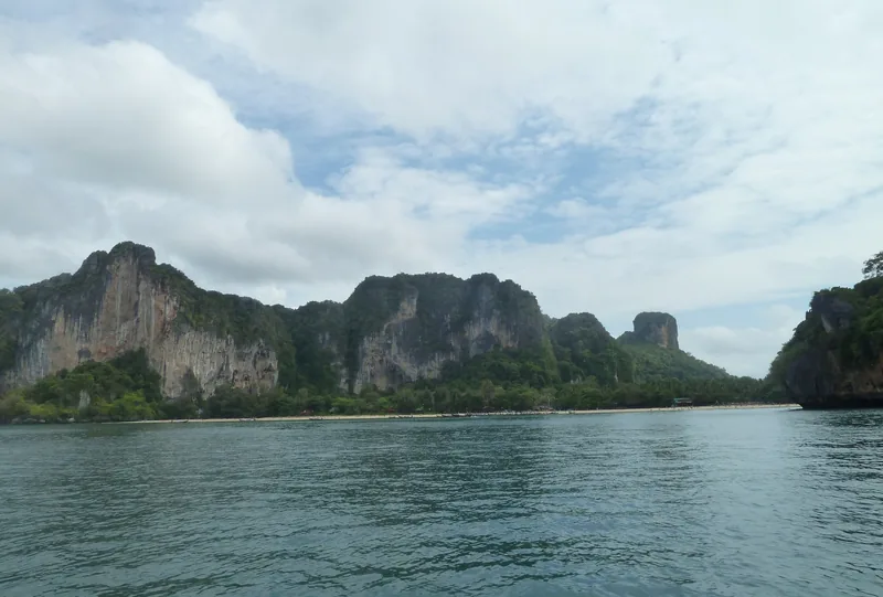 Limestone cliffs rise above a sandy beach along the coastline near Krabi, Thailand.