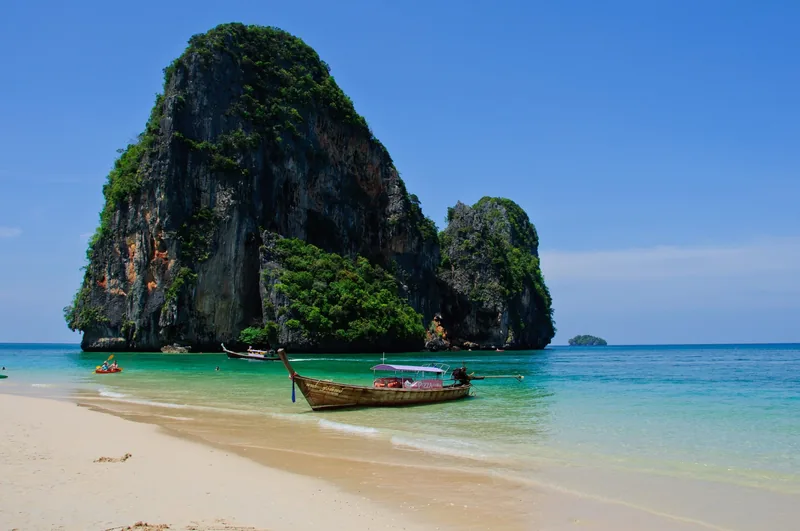A longtail boat rests on the sandy shore of Phra Nang Beach beneath a towering limestone karst in Krabi.