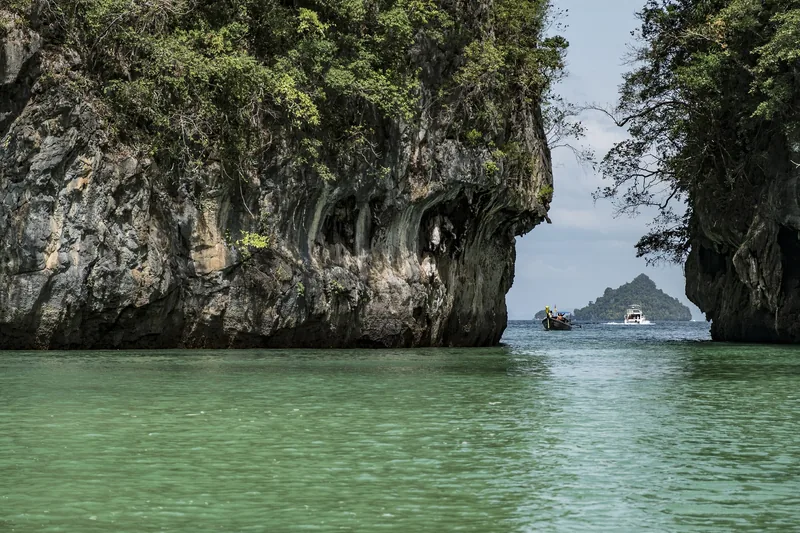 Limestone cliffs frame a turquoise lagoon and distant island near Krabi, with boats passing through the channel.