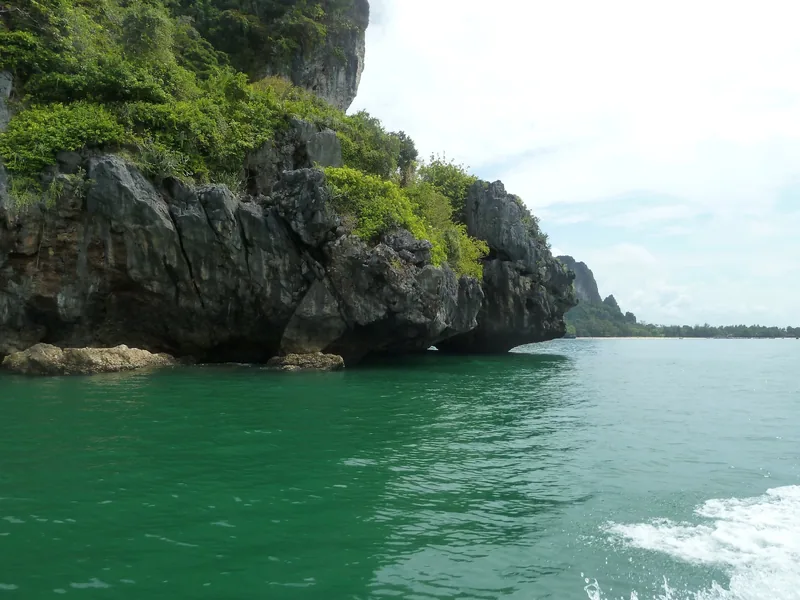 Limestone cliffs covered in greenery rise above turquoise water near Railay Beach in Krabi, Thailand.