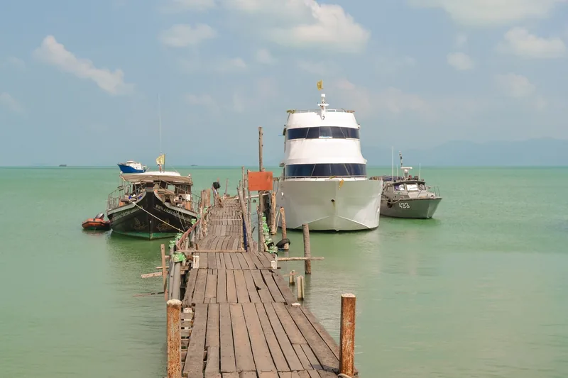 A wooden pier stretches over turquoise water toward moored boats near Bophut village in Koh Samui.