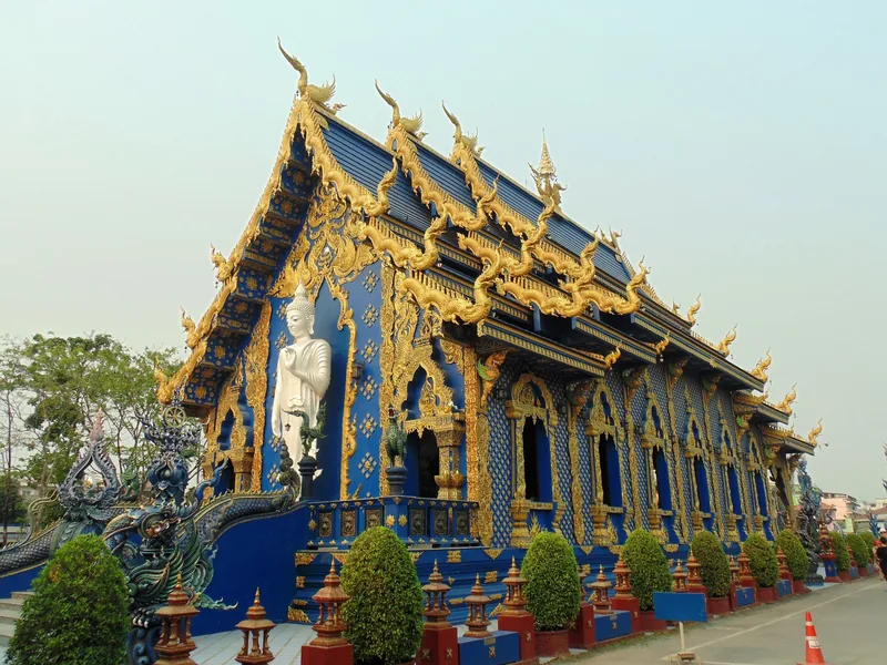 A blue and gold ornate temple with a white standing Buddha statue at Wat Rong Suea Ten in Chiang Rai.