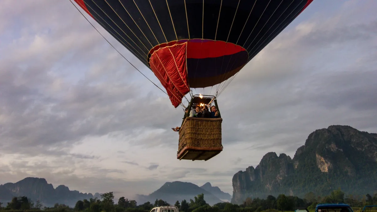 A hot air balloon with a basket of passengers rises over the limestone karsts of Vang Vieng at dawn.