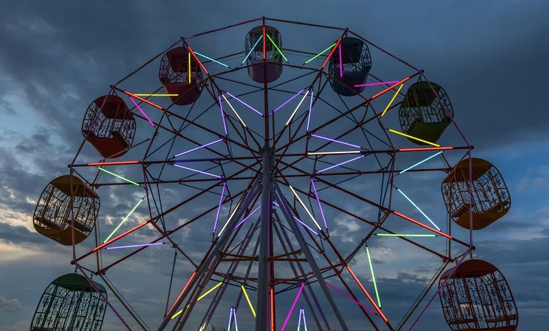 A colorful illuminated ferris wheel glows against a dusky cloudy sky in Vientiane.