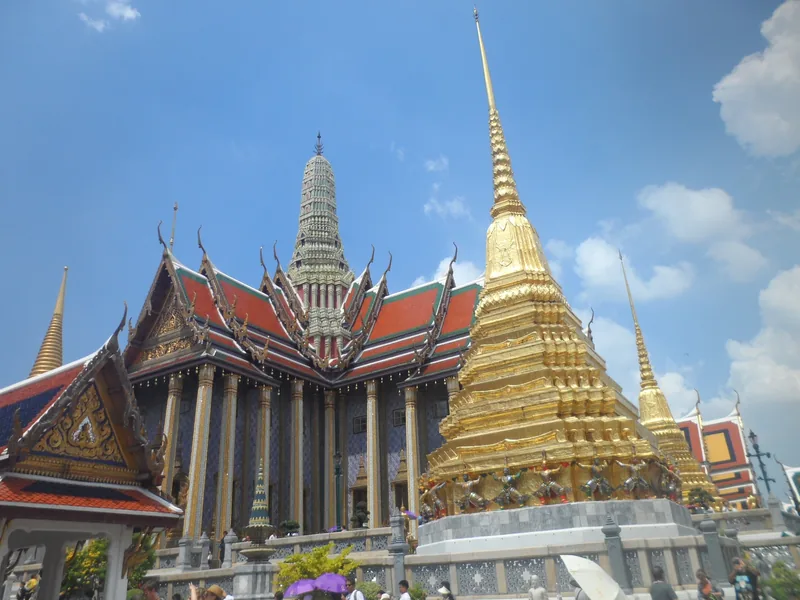 Golden chedi and ornate roofs of the Grand Palace complex rise against a blue sky in Bangkok.