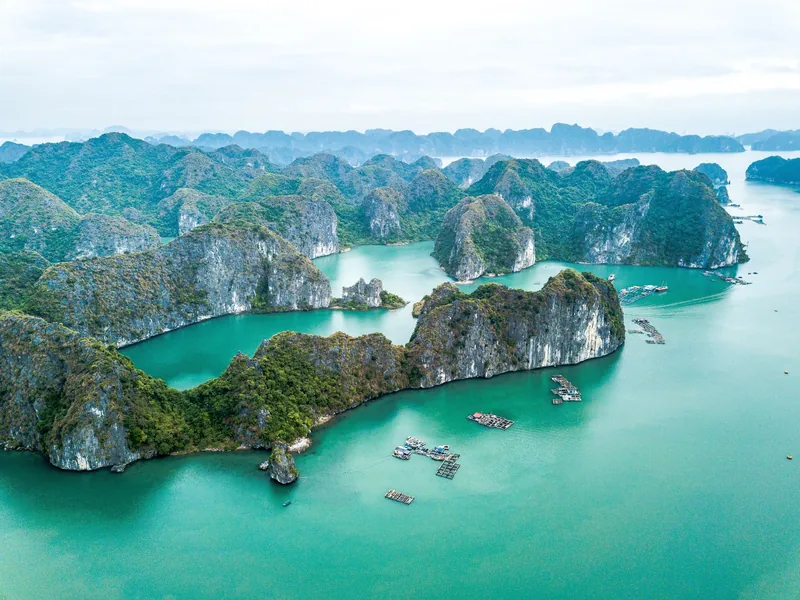 Aerial view of limestone karsts rising from turquoise water with floating fish farms in Ha Long Bay