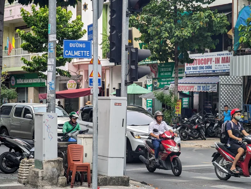 Motorbikes and cars pass a street sign for Đường Calmette amid shops in District 1, Ho Chi Minh City.