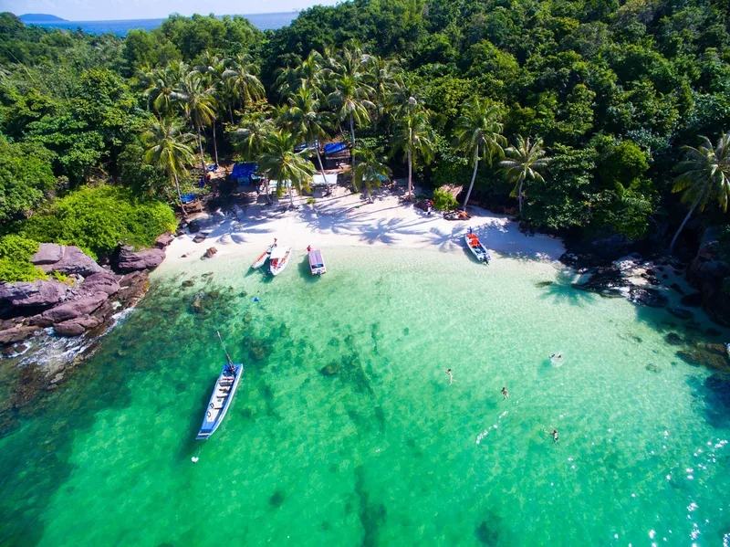 Aerial view of turquoise water, white sand, and moored boats along a palm-fringed cove in Phu Quoc.