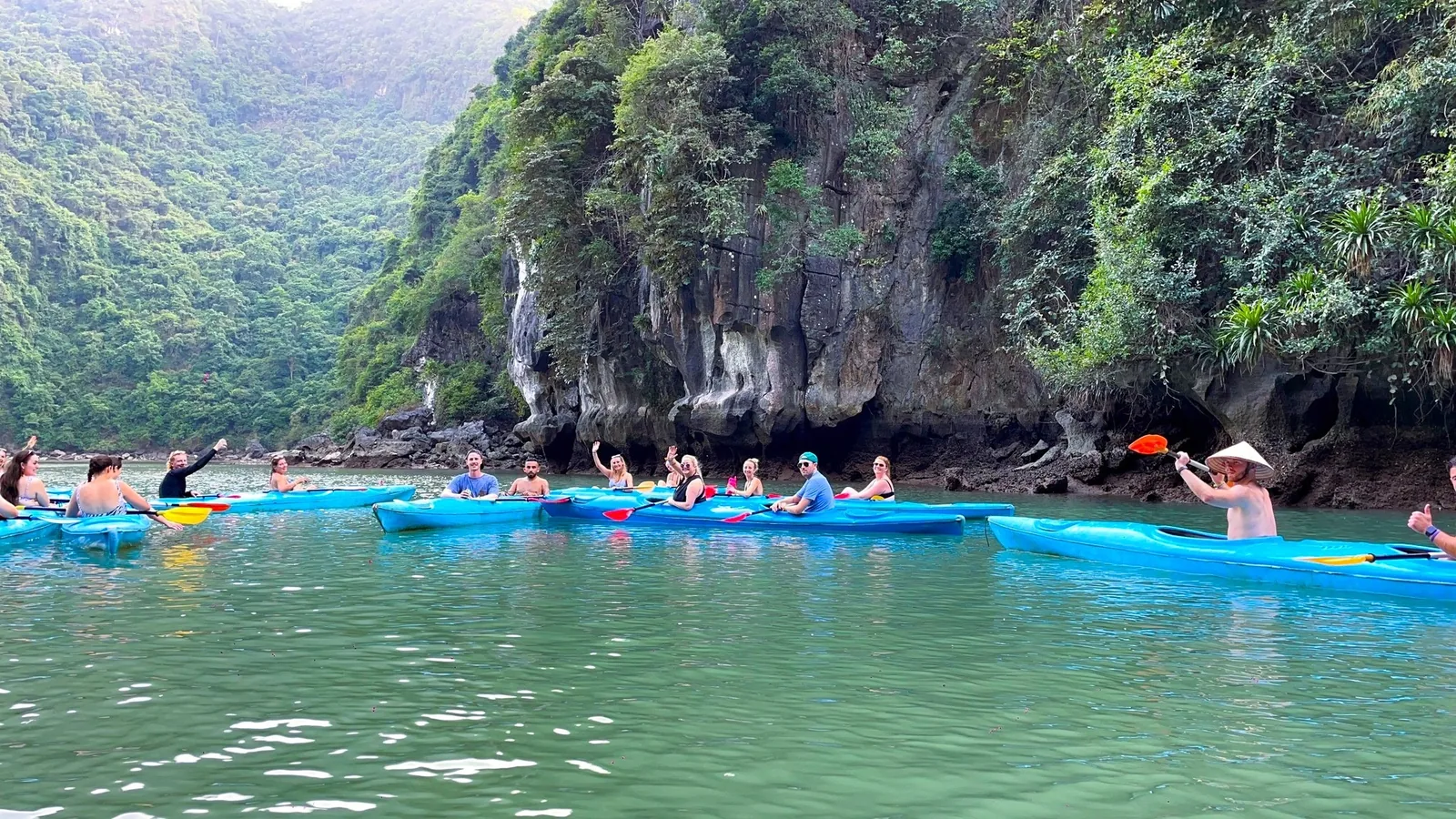 Tourists paddle blue kayaks past limestone cliffs in Lan Ha Bay near Cat Ba Island.
