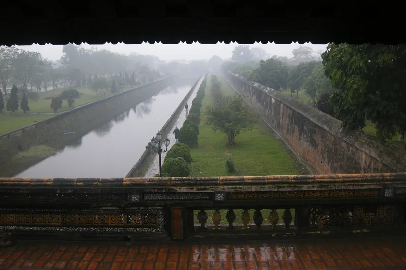 A misty moat runs alongside the ancient stone walls of the Imperial City in Hue, viewed from a gate pavilion.