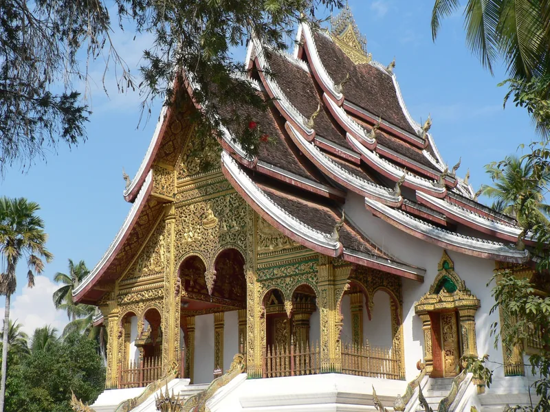 A gilded Buddhist temple with tiered roofs stands within the royal palace grounds in Luang Prabang, Laos.