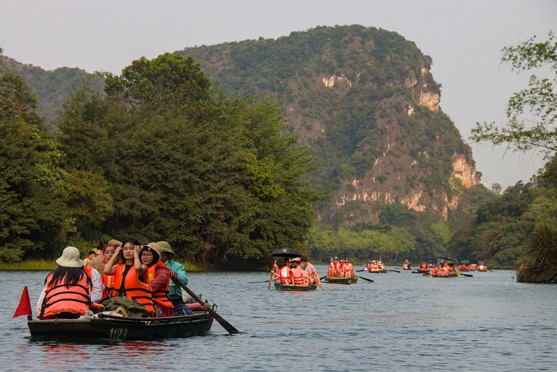 Tourists in orange life jackets ride small boats past limestone karsts on the river at Trang An, Ninh Binh.