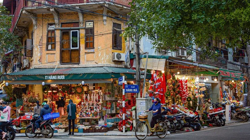 A weathered corner building on Hàng Mã street in Hanoi's Old Quarter, decked with colorful festive decorations and busy.