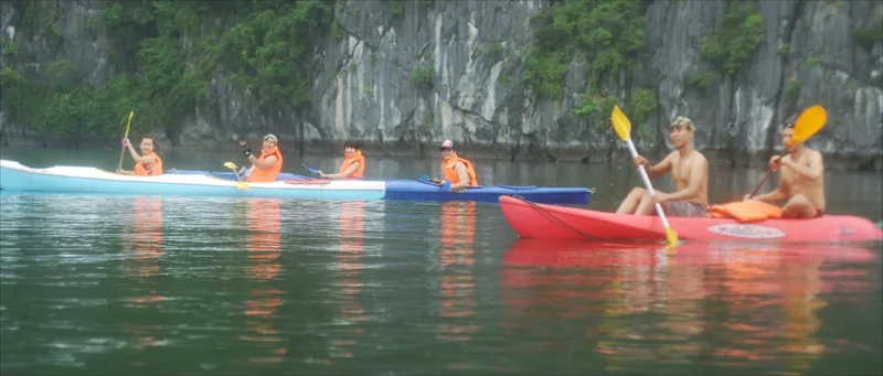 Kayakers in colorful boats paddle beneath limestone cliffs in Lan Ha Bay near Cat Ba.