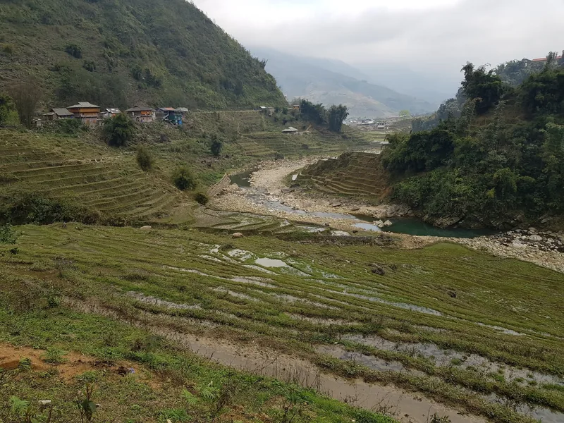 Terraced rice fields and a rocky stream wind through a misty valley near Ta Van village in Sapa, Vietnam.