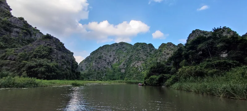 A small boat drifts along a calm river between limestone karst mountains at Tam Coc in Ninh Binh.