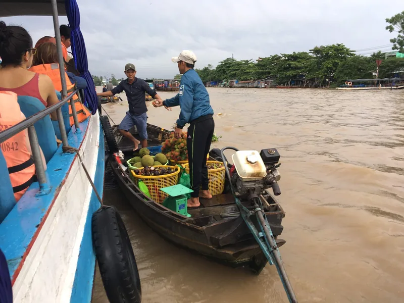 Vendors sell fruit baskets from a small boat to tourists on a larger boat at Cai Rang floating market, Can Tho.
