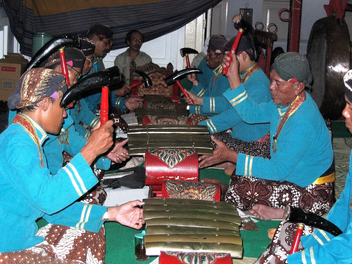 Musicians in traditional blue attire play saron gamelan instruments during a performance in Yogyakarta.