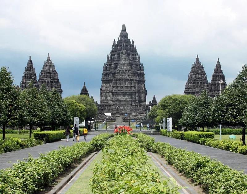 Towering stone spires of Prambanan temple rise beyond manicured gardens near Yogyakarta.